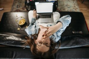Overhead view of a woman eating chips while working on a laptop, illustrating remote work lifestyle.